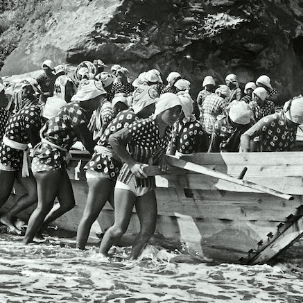 ca. 1947, Toba, Japan --- Pearl divers start to push their boats from the beach into Toba Bay. The young women harvest oysters implanted with pearls for the Mikomoto company. --- Image by © Horace Bristol/CORBIS